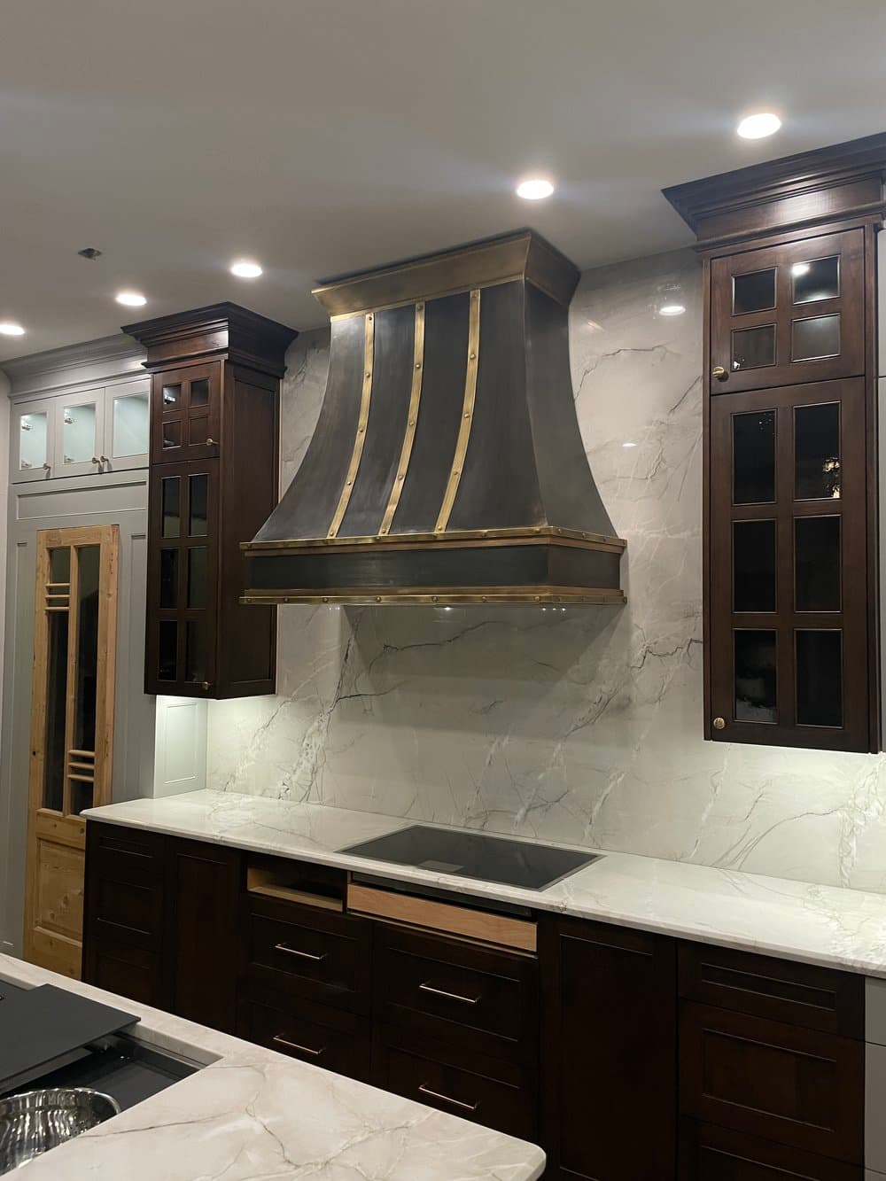 Dark Monarch range hood with brass banding against a marble backsplash in a Southlake, Texas kitchen