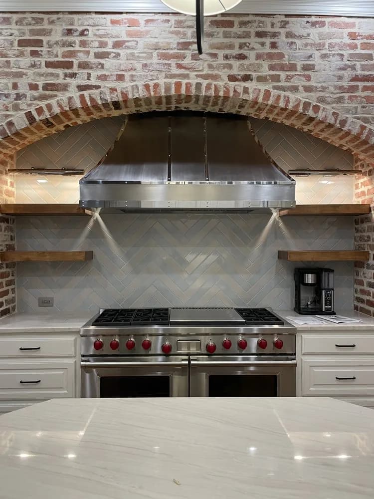 Brushed stainless steel range hood set inside an exposed brick arch above a professional range